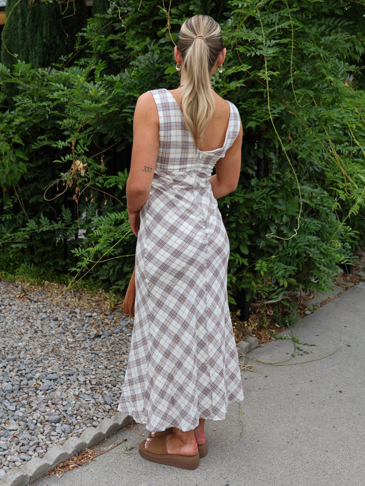Woman in a plaid dress walking away from the camera with greenery in the background