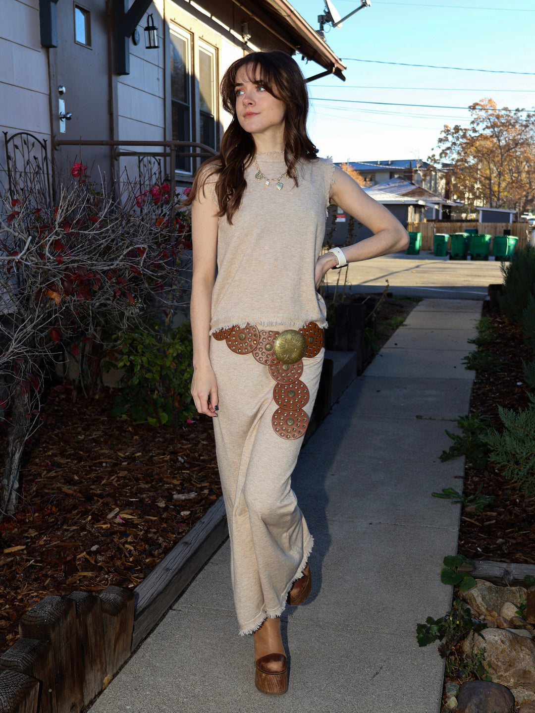 Woman in a beige sleeveless top and long skirt with a decorative belt walking outdoors.