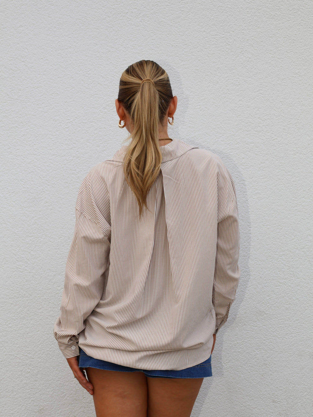 Person wearing a beige striped shirt and blue shorts against a light gray wall