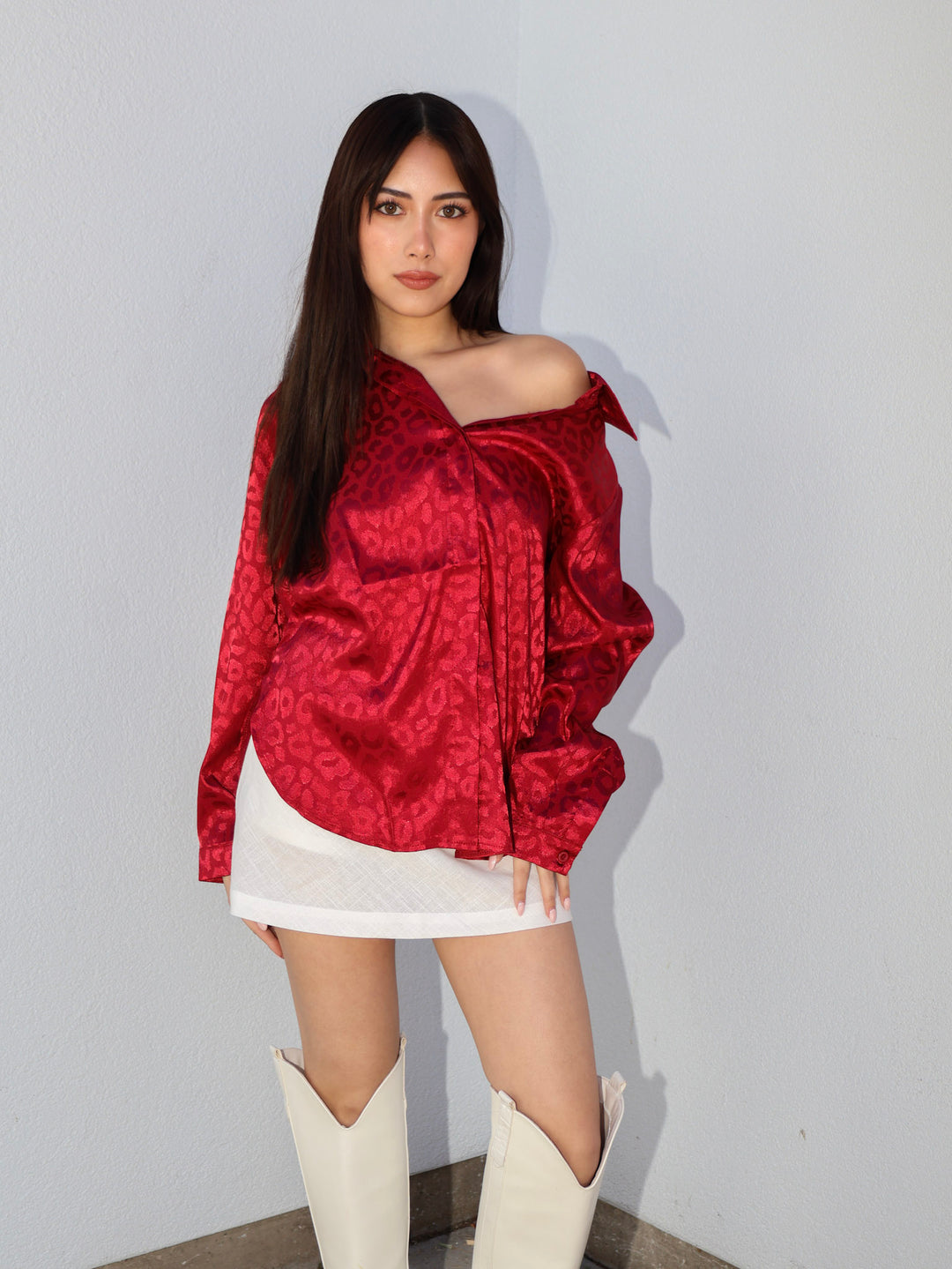 Woman wearing a red off-shoulder top and white skirt with high boots against a plain background