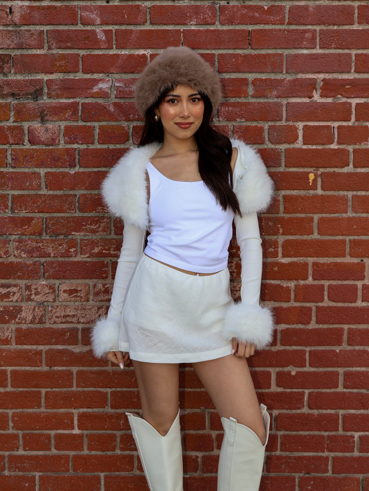 Person wearing a white outfit with fur accents against a brick wall