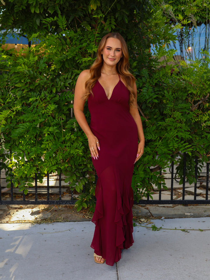 Woman in a burgundy dress standing in front of green bushes