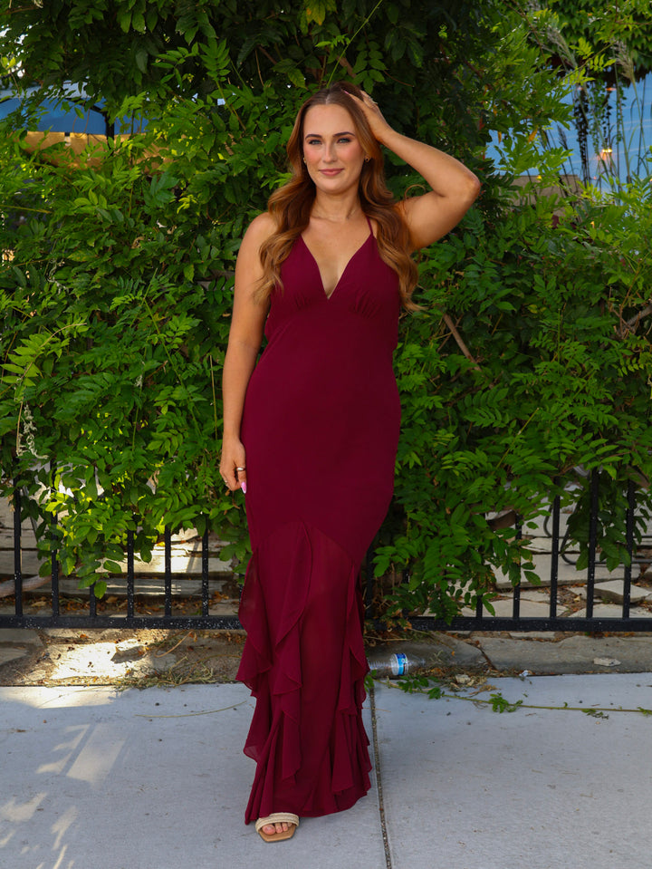 Woman in a burgundy dress standing outdoors with greenery in the background