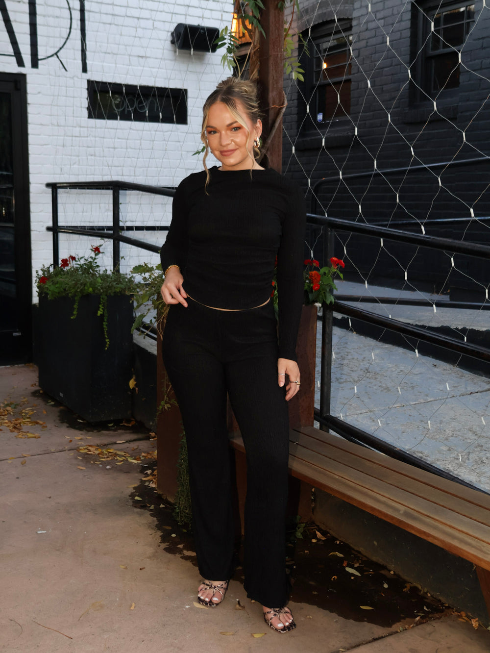 Woman in a black outfit standing in front of a building with a decorative wire fence.