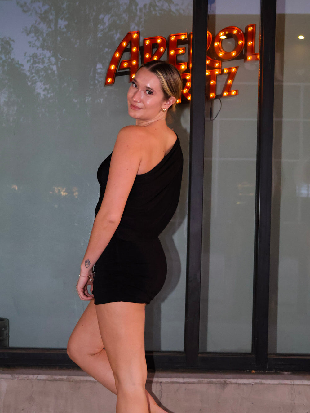 Woman in a black dress standing in front of a glass door with sign.
