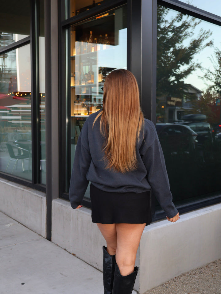 Person wearing a dark sweater and a black skirt walking past a building with large windows.