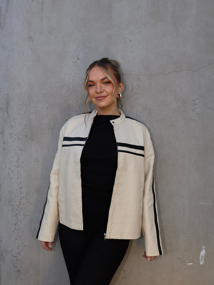 Woman wearing a white jacket with black stripes against a gray concrete wall