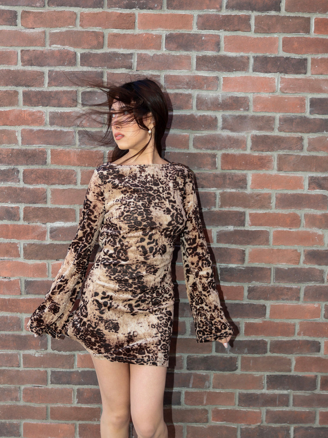 Person wearing a patterned dress standing against a brick wall
