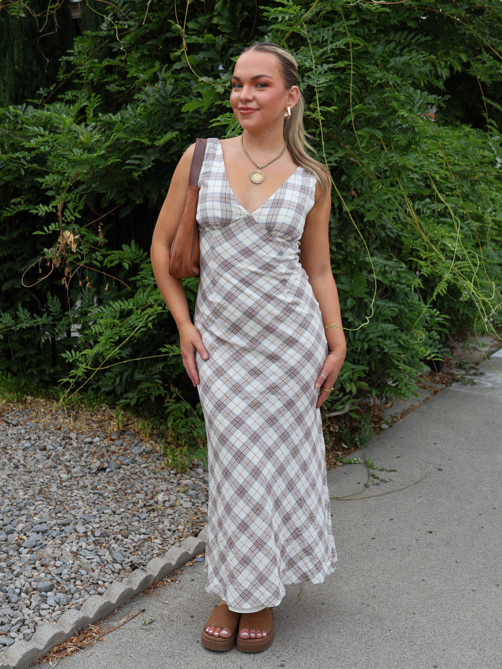 Woman wearing a plaid dress standing outdoors with greenery in the background