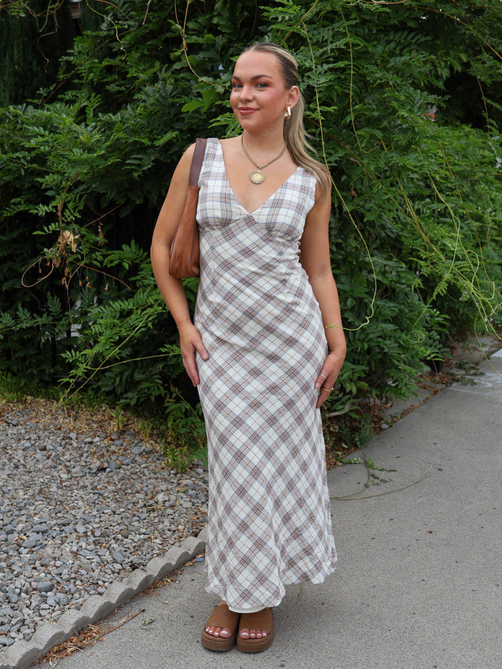Woman wearing a plaid dress standing outdoors with greenery in the background