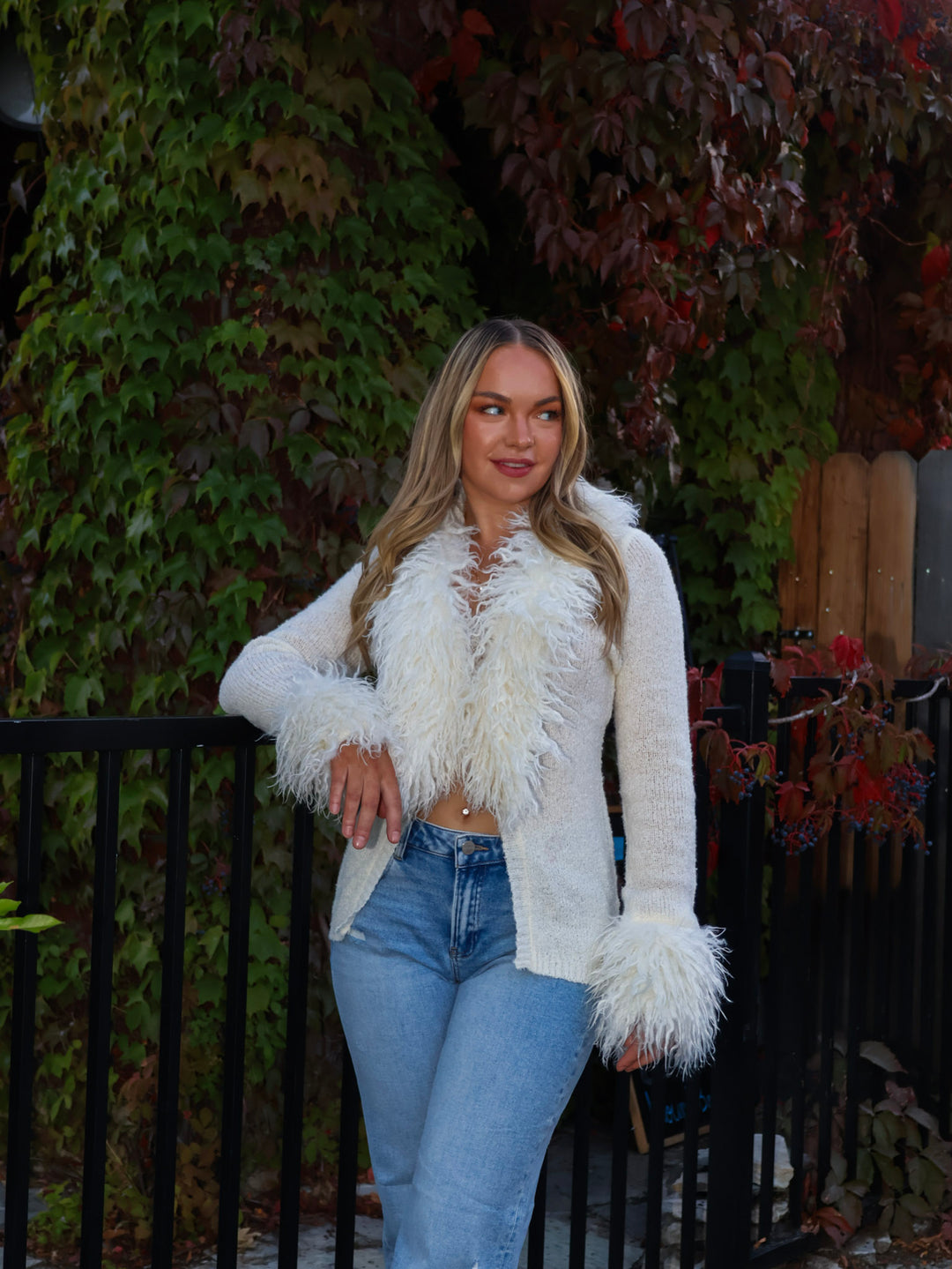 Woman wearing a white fluffy jacket and blue jeans standing outdoors.
