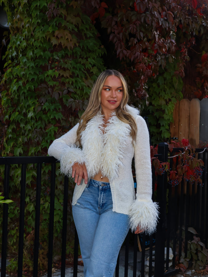 Woman wearing a white fluffy jacket and blue jeans standing outdoors.