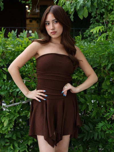 Woman wearing a brown strapless dress standing in front of green foliage