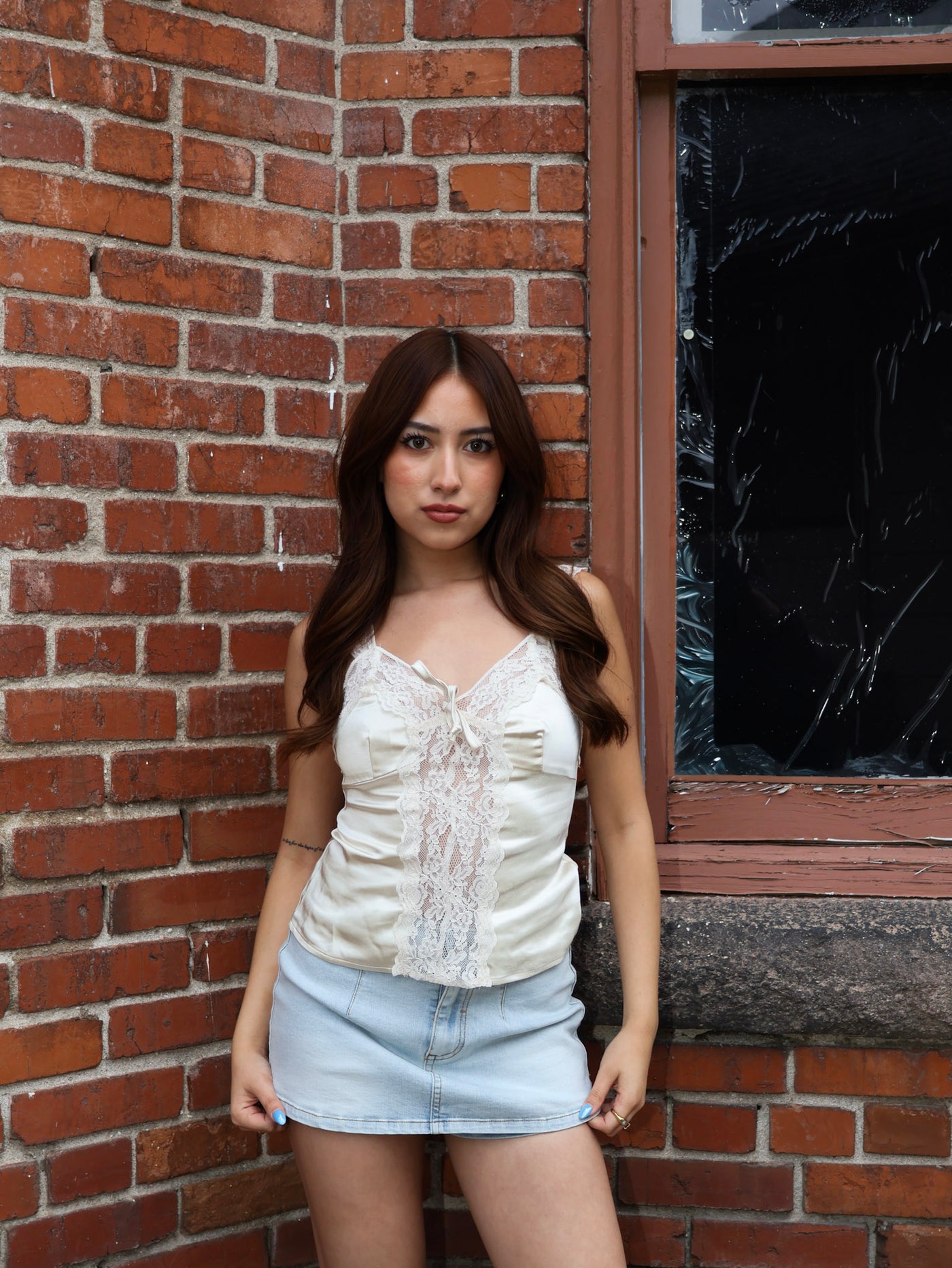 Woman standing against a brick wall with a window in the background