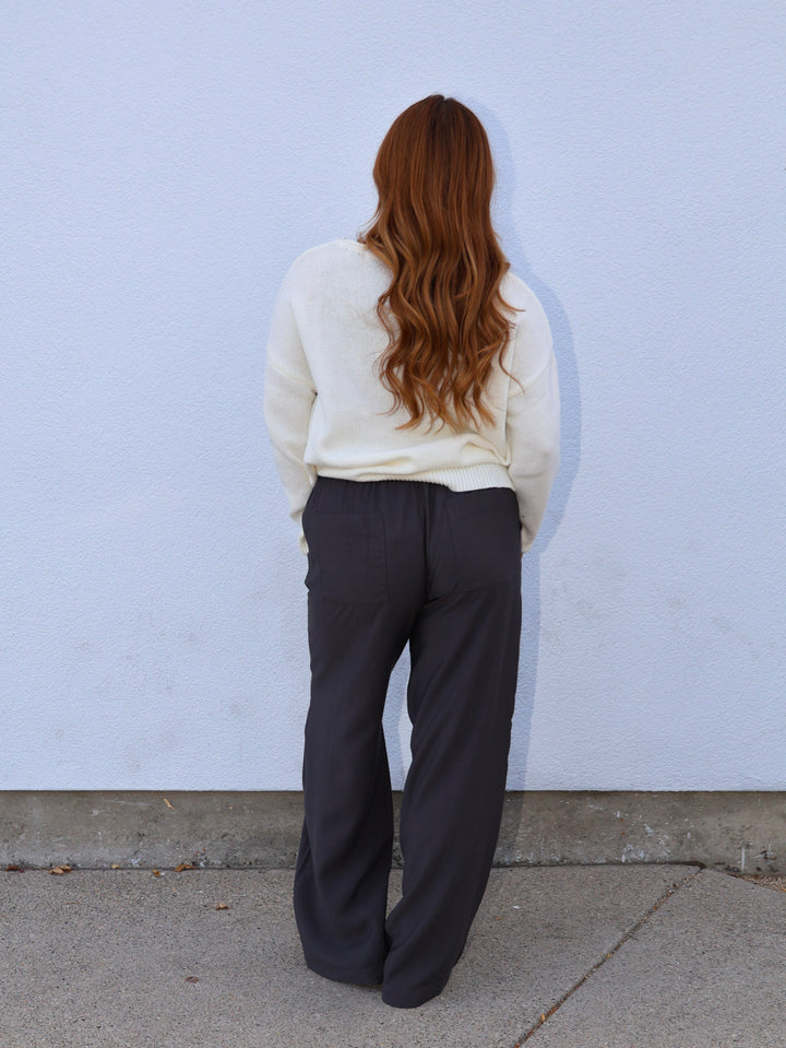 Person wearing a cream sweater and dark pants against a light blue wall.