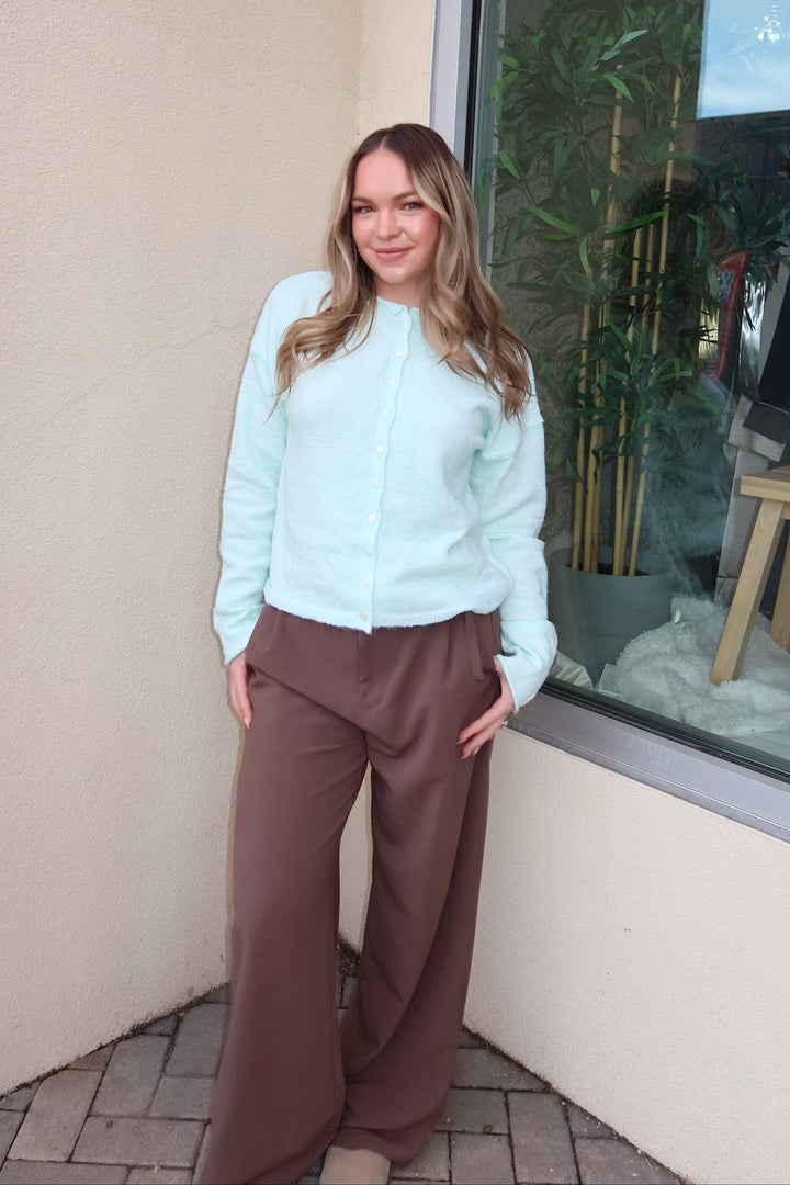 Person standing on a beige surface with a glass door and plants in the background