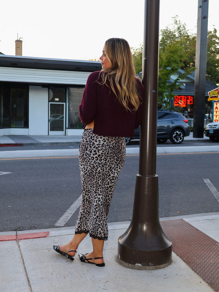 Woman in leopard print pants and maroon sweater standing on a sidewalk next to a streetlight.