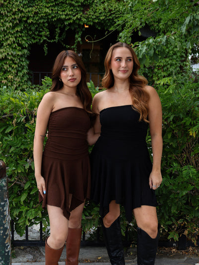 Two women wearing strapless dresses standing outdoors with greenery in the background