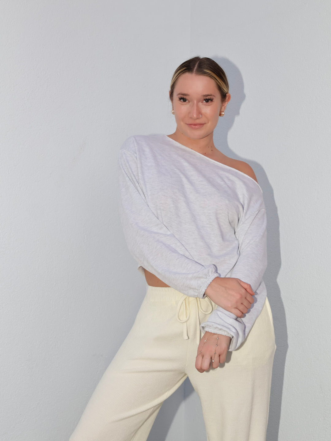 Person wearing a white one-shoulder top and cream pants against a plain background