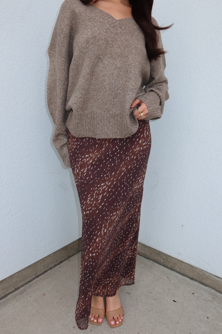 Cropped front view of the burgundy print Bambi fluid maxi slip skirt, worn with an oversized taupe sweater and tan sandals