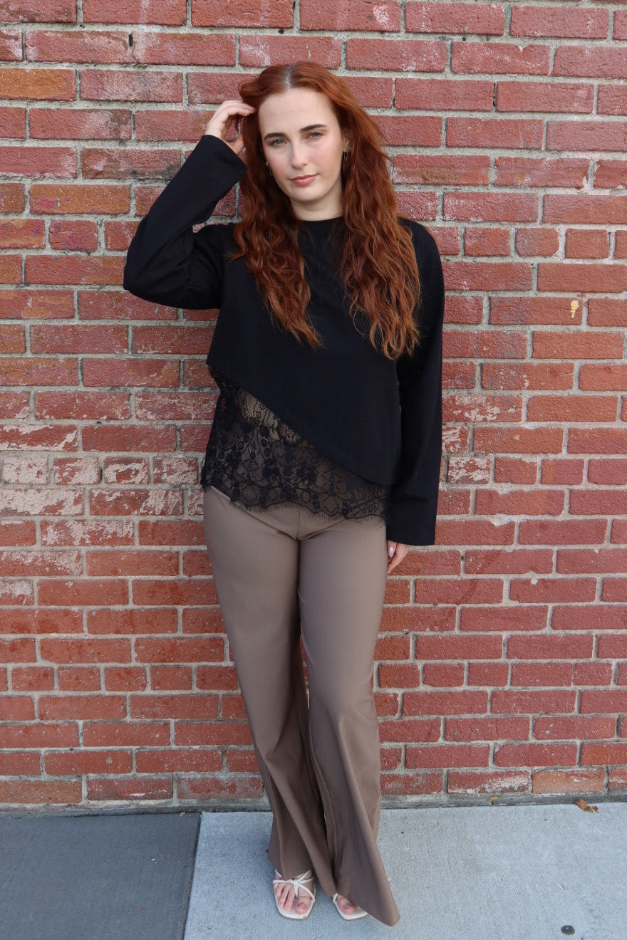 Model wearing the taupe Billie tailored wide leg trousers with a black lace hem top, hand in her hair