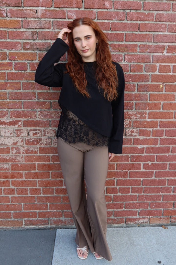 Model wearing the taupe Billie tailored wide leg trousers with a black lace hem top, hand in her hair