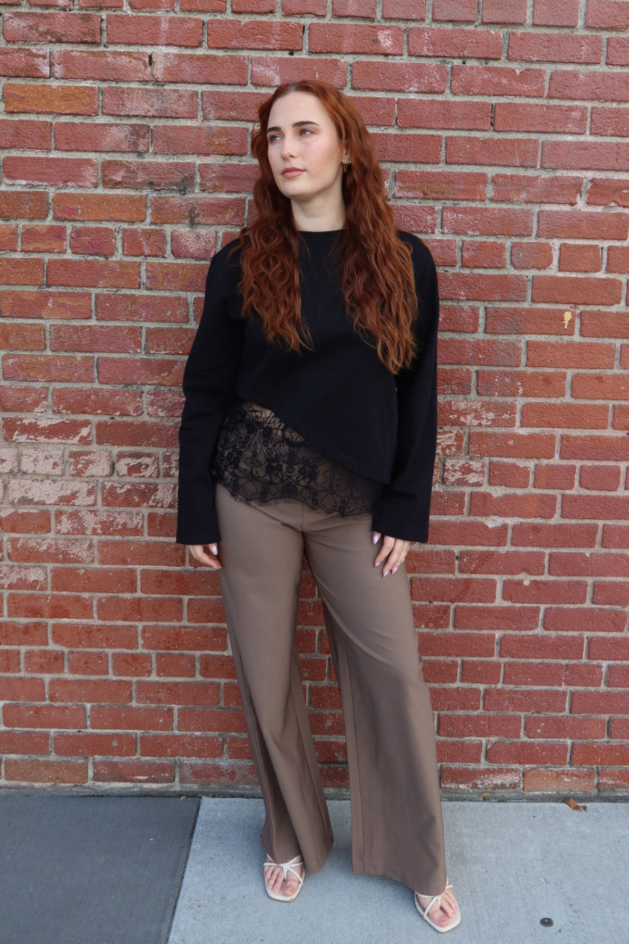 Front view of the black Charlie asymmetric lace trim top worn with the taupe Billie tailored wide leg trousers and sandals