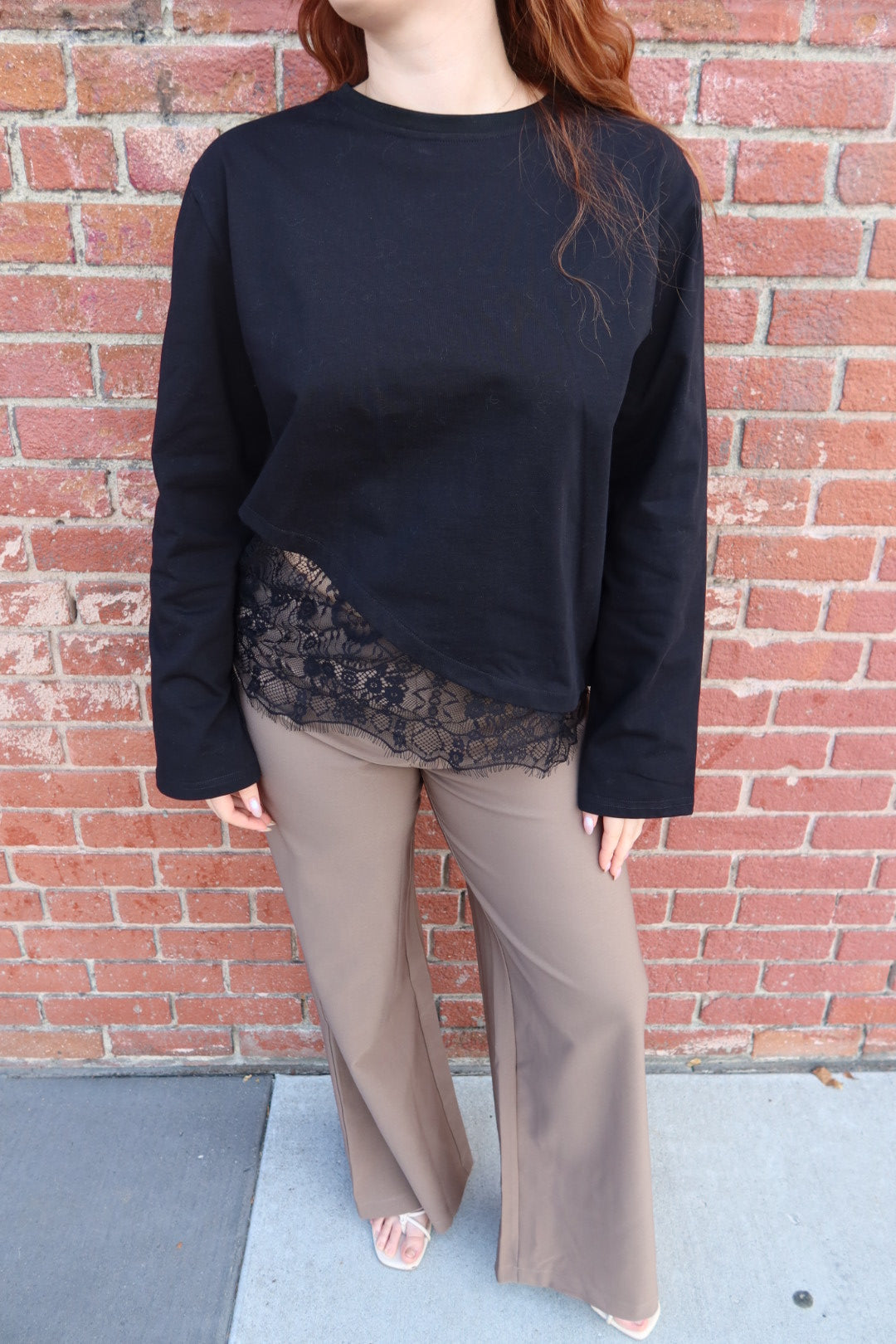 Close front view of the black Charlie asymmetric lace trim top, showing the angled lace hem, worn with taupe trousers