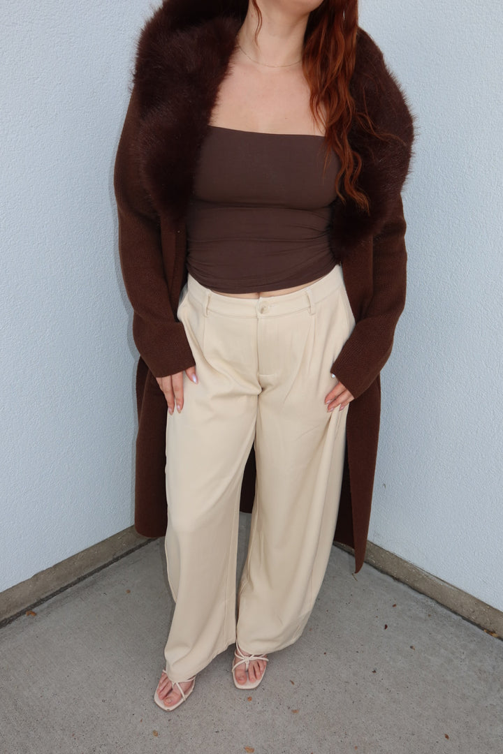 Model with hands on hips in the cream Louis pleated barrel wide leg pants and a long brown cardigan