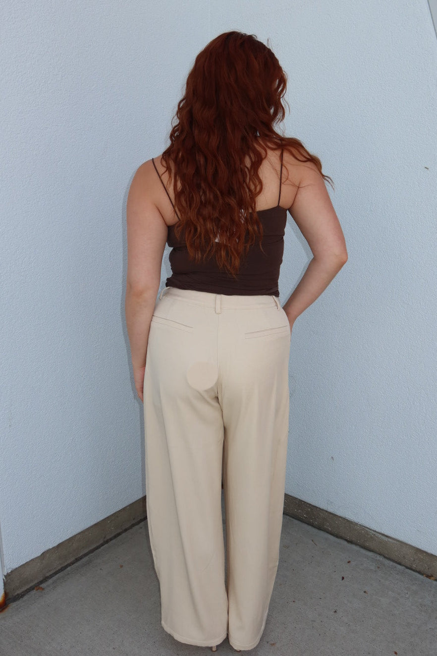 Back view of the cream Louis low waist pleated barrel wide leg pants with a brown cami, showing the wide leg and back pockets