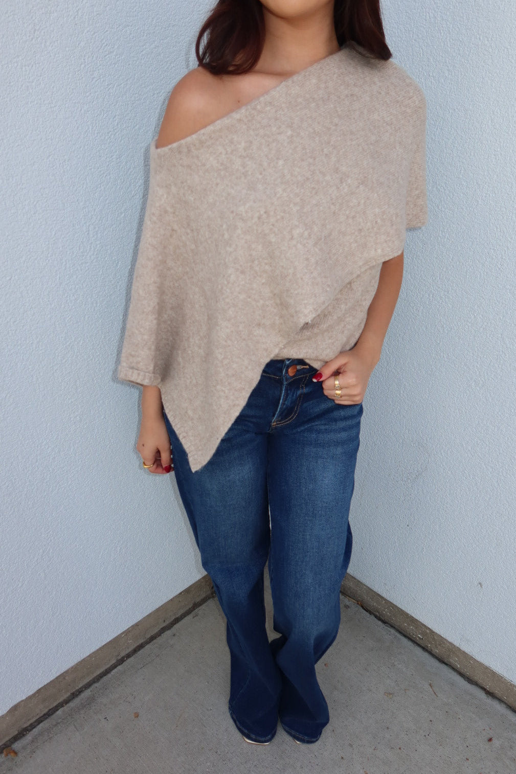 Close front view of the oatmeal Ainsley off shoulder asymmetric knit poncho sweater, showing the one-shoulder neckline