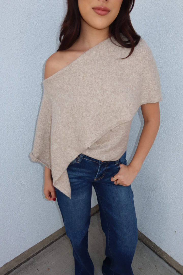 Close view of the oatmeal Ainsley off shoulder asymmetric knit poncho sweater, showing the off shoulder drape