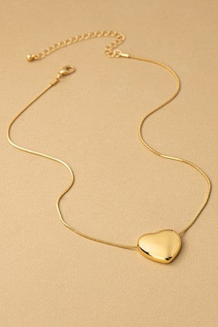 Gold necklace with a heart-shaped pendant on a beige background