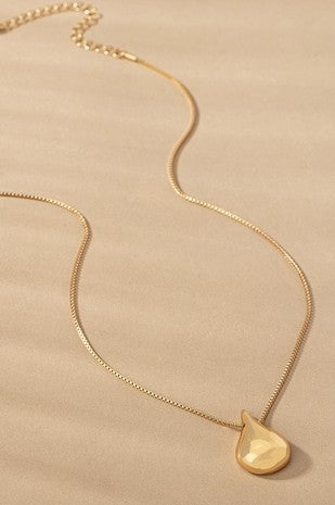 A gold-colored puffy teardrop pendant necklace with a box chain design laid out on a flat surface.